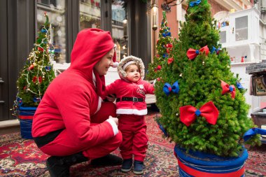 Noel aile tatili konsepti. Mutlu Noeller ve mutlu tatiller. Anne ve kızı Noel Baba kostümü giymiş. Eğlenceli yürüyüşler. Anne kızını kollarında tutuyor, samimi bir gülümseme..