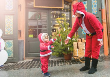 Noel aile tatili konsepti. Mutlu Noeller ve mutlu tatiller. Anne ve kızı Noel Baba kostümü giymiş. Eğlenceli yürüyüşler. Anne kızını kollarında tutuyor, samimi bir gülümseme..