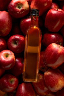 Elma sirkesiyle dolu bir şişe çok sayıda taze kırmızı elmayla kaplı bir yüzey üzerinde duruyor. Ayarlar gündüz vakti doğal ışık alan bir mutfağı gösteriyor..