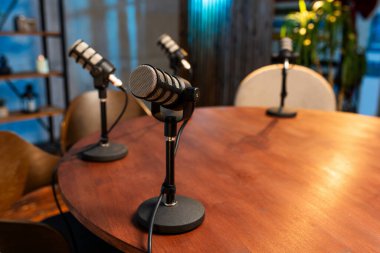 Modern bir odada tahta bir masada dört mikrofon duruyor. Ayar podcast kaydı için hazır. Boşluğun basit ve temiz bir tasarımı var..