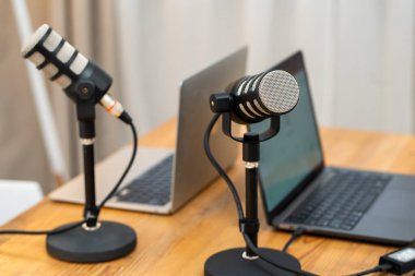 Bir dizüstü bilgisayarın yanındaki masada iki mikrofon duruyor. Sahne, bir podcast için röportaj yapmak için kullanılan bir çalışma alanını gösteriyor. Atmosfer ses kaydına odaklanmış durumda..