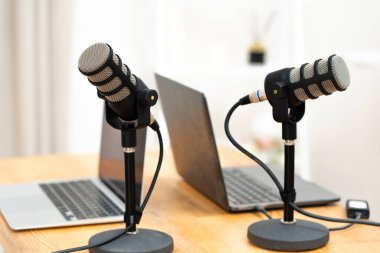 Tahta bir masanın üzerine iki mikrofon yerleştirildi. Her mikrofonun önünde bir dizüstü bilgisayar açık. Bu ayar bir ofiste bir podcast ya da röportaj oturumunu gösterir.