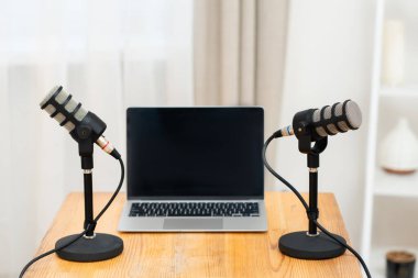 İki mikrofon, aralarında dizüstü bilgisayar olan ahşap bir masada duruyor. Basit bir ofis ortamında podcast röportajı için hazırlar. Bu kurulum eğitim veya eğitim için bir oturum önerir.