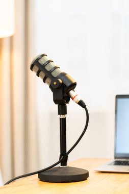 Ev ofisindeki bir dizüstü bilgisayarın yanında bir mikrofon duruyor. Bu kurulum, eğitim konularına odaklı bir podcast röportajını kaydetmeye hazır. Alan basit ve işlevsel..