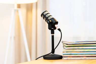 Ev ofis alanındaki bir masada bir mikrofon duruyor. Yakınlarda, birkaç kitap düzgünce istiflenmiş. Bu kurulum bir podcast röportajını kaydetmek için. Yumuşak ışık odayı dolduruyor..