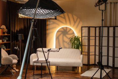 Bir podcast kayıt alanı röportaj için ayarlanmış kanepe ve mikrofonları olan rahat bir stüdyo gösteriyor. Yumuşak ışıklandırma tartışmalar için bir karşılama alanı yaratır. Kayıt oturumu için ekipman ayarlandı.