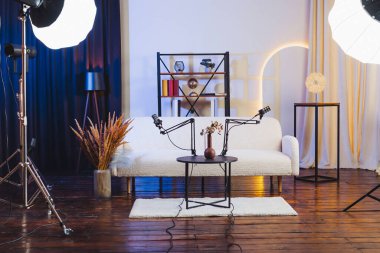 Bir stüdyoda bir podcast röportajı bir masanın üzerine kurulmuş iki mikrofonla yapılır. Mekanda bir kanepe ve dekoratif eşyalar var. Parlak ışıklar sahneyi aydınlatır.