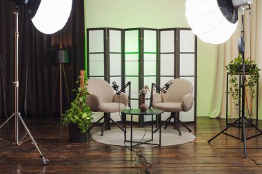 Podcast kaydı için stüdyoda iki sandalye ayarlanır. Sandalyelerin önüne iki mikrofon yerleştirildi. Ayar yumuşak ışıklandırmalı ve bitkilerle dolu..