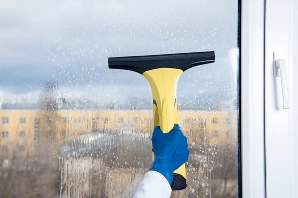 The yellow device collects drops of water and cleans the window. Wiper in the hand. Business washing and cleaning windows.