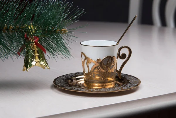 Christmas coffee concept. Golden coffee cup, bell and new year tree branch on table in cafe. Luxurious elegance style.
