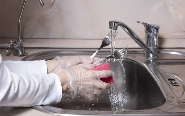 女人们的手 用手套洗碗 厨房的水龙头在金属槽上用淡水洗碗 人洗银金属叉 用海绵紧握双手 — 图库照片