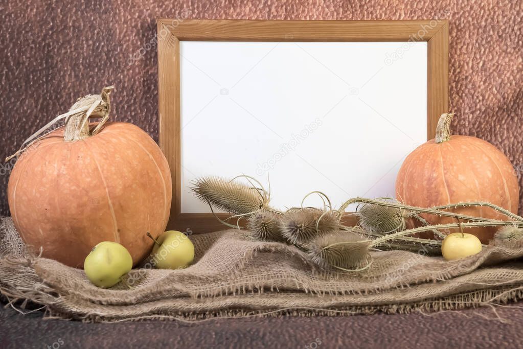 Portrait empty wooden frame mockup with pumpkins, yellow apples and dry grass on sackcloth. Brown background. Thanksgiving, Halloween concept.