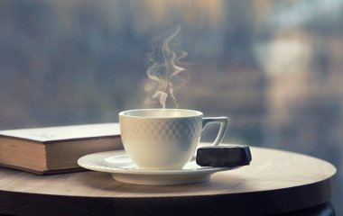 Kahve masasında beyaz kahve fincanı ve kahverengi kitap. Sonbahar sonu ve konfor konsepti. Pencere manzaralı. Seçici odak.