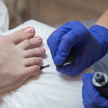 Bir pedikür uzmanı pembe cila ile ayak tırnaklarını boyuyor. Mavi eldivenli eller. Salon pedikür. Pedikür güzellik salonu konsepti.