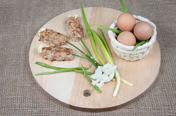 Food art idea for Easter. Flowers made of meat on wooden cutting board, easter basket with eggs on natural burlap background.