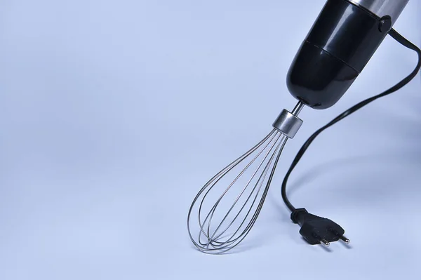 Stylish black kitchen mixer on blue background. Professional steel electric mixer with metal whisk and plug.