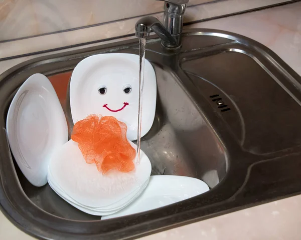 Good washed dishes in kitchen sink. Smiling white plate with eyes and happy emotion.