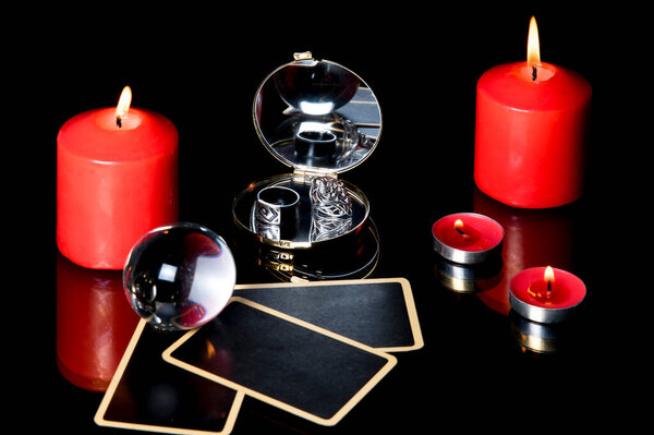 Red candles, mirror, rings and tarot cards isolated on black background. Divination still life by candlelight at evening. Magic ritual. Mystical atmosphere of fortune telling. Esoteric. 