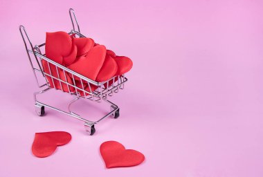 Alışveriş arabasının içinde kırmızı kalpler. Kırmızı kalplerle dolu mini tramvay. Sevgililer günü için tebrik kartı, tatil, düğün ya da doğum günü pembe arka planda. 