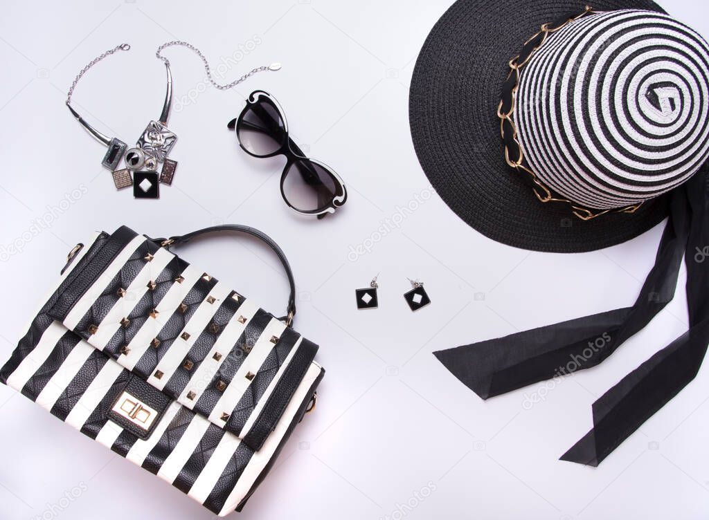 Striped women's hat, glasses, earring, necklace, black and white purse with stripes on white background. Flat lay, top view. Modern fashion style