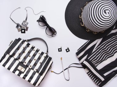 Çizgili kadın şapkası, gözlük, küpe, kolye, pantolon, beyaz arka planda çizgili siyah beyaz çanta. Düz yerde, üst tarafta. Modern moda tarzı