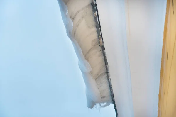 Ice and snow covers roof building, dangerous ice dams hanging from roof.  Danger and safety concept