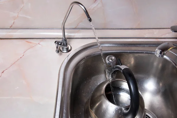 Pouring filtered water into kettle from water filter. Closeup of sink and faucet. Drinkable water in kitchen