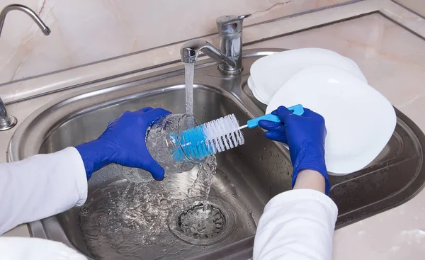 女人们的手 戴着蓝色手套 在厨房水龙头边的金属水池上洗玻璃瓶 用刷子和白盘合拢手 — 图库照片