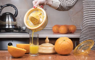 Kadınların eline yakın çekim taze portakal suyu yapıyor. Portakal suyunu bardağa döküyorum. Kadın eli portakal suluyor..