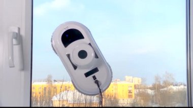 Ev yapımı elektrikli süpürge robotu odada cam yıkıyor. Mavi gökyüzü ve sarı bina dışarıda. Pencereleri temizleyen robot yardımcısı