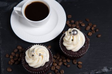 Siyah arka planda iki kek ve beyaz kahve fincanı, kremalı ev yapımı kek ve kavrulmuş kahve çekirdeği.. 