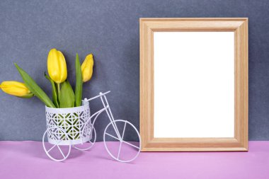 Boş fotoğraf çerçevesi ve bir buket sarı lale çiçekli oyuncak bisiklet. Pembe ve gri arka plan tasarımın için bir model. Boşluğu kopyala
