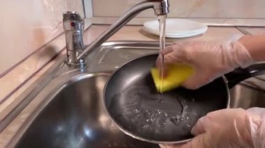 Kadın damlayan tavayı yıkıyor. Sünger temizleme tavasıyla elini kapat. Mutfağa su dök.