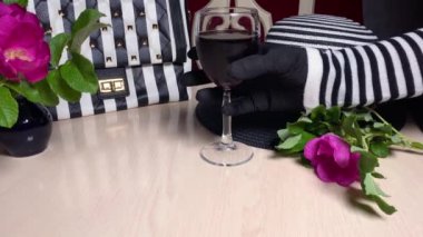 Çizgili şapka, siyah beyaz çanta ve çizgili masa. Şarap kadehini kırmızı şarapla tutan kadın eli. Modern moda tarzı