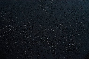 Su damlaları siyah cam arka planda izole edilmiş. Yağmur dokusu