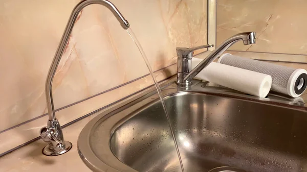 Pouring filtered water from water filter. Closeup of sink and faucet. Drinkable water in kitchen