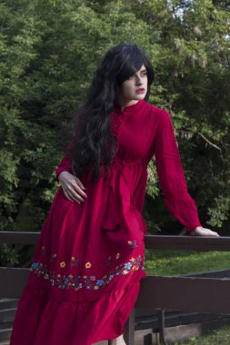 Uzun kollu kırmızı boho elbiseli güzel bir kız köprüdeki parkta yürüyor.