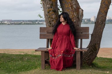 Parkta uzun kollu kırmızı boho elbiseli güzel bir genç kız yürüyor.