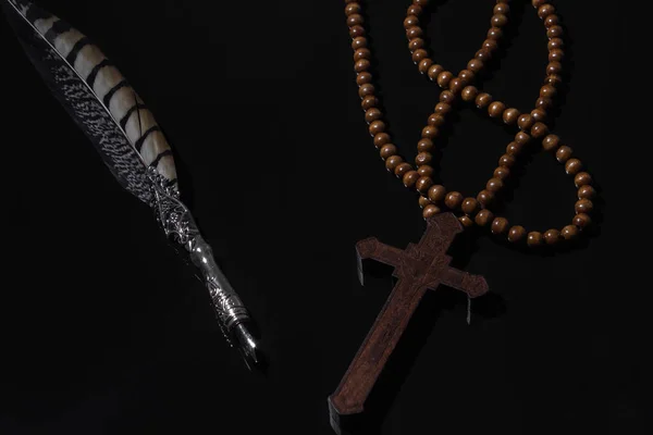 wooden religious cross and vintage Feather quill pen on black background. Concept photo on religion and science