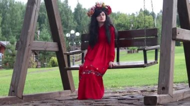 Kırmızı etnik elbiseli bir kız parkta bir salıncakta oturuyor.