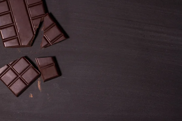 Siyah arka planda kırılmış siyah çikolata parçaları. Üst görünüm.
