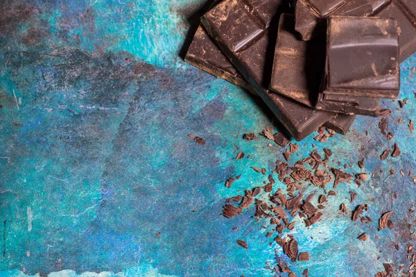 Broken pieces of dark chocolate on blue abstract background. Top view.