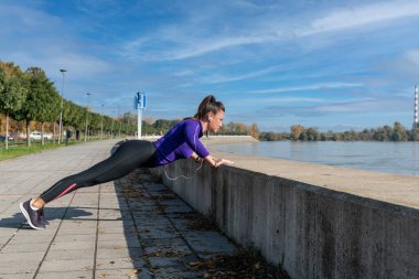 Genç, yakışıklı, aktif, sportif bir kadın. Açık hava egzersizi olarak nehir kenarında şınav çekiyor.
