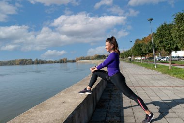 Genç aktif atletik kadın dışarıda koşmak için bacak kaslarını esnetiyor. 