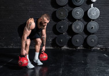 Genç, aktif, güçlü, terli, iri kaslı, kaslı, sırt kaslarını çalıştıran, spor salonundaki kettlebell 'lerle sıkı bir çapraz antrenman yapan adam.