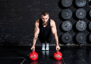 Genç, aktif, terli, formda, kaslı, kaslı bir adam spor salonundaki kettlebell 'lerde şınav çekiyor.