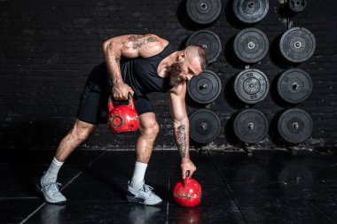 Genç, aktif, güçlü, terli, iri kaslı, kaslı, sırt kaslarını çalıştıran, spor salonundaki kettlebell 'lerle sıkı bir çapraz antrenman yapan adam.