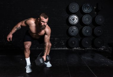 Genç, aktif, terli, formda, kaslı, iri kaslı, kuku kaldıran ya da spor salonunda dambıl ağırlığıyla antreman yapan kaslı bir adam.