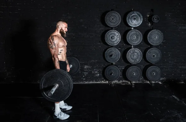 Genç, aktif, terli, güçlü, güçlü, kaslı, halter ağırlıklı, halter kaldıran, ağırlık kaldıran ve spor salonunda ağırlık kaldırma antrenmanına başlayan kaslı bir adam.