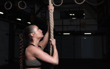 Genç, aktif, güçlü, terli, kaslı, çekici ve pozitif güçlü kız halata tırmanmaya hazırlanıyor.